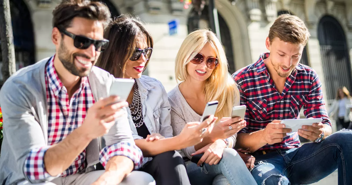 A group of people sitting on a bench looking at their phones