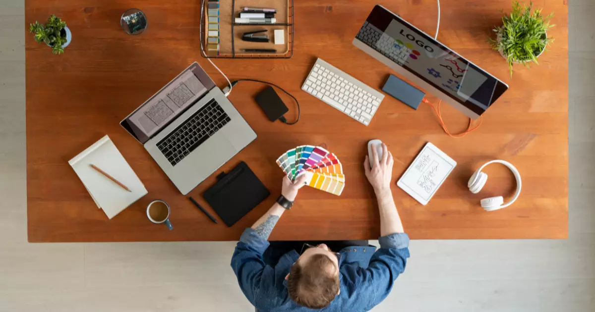 A person holding a color swatch with laptop and computer in front