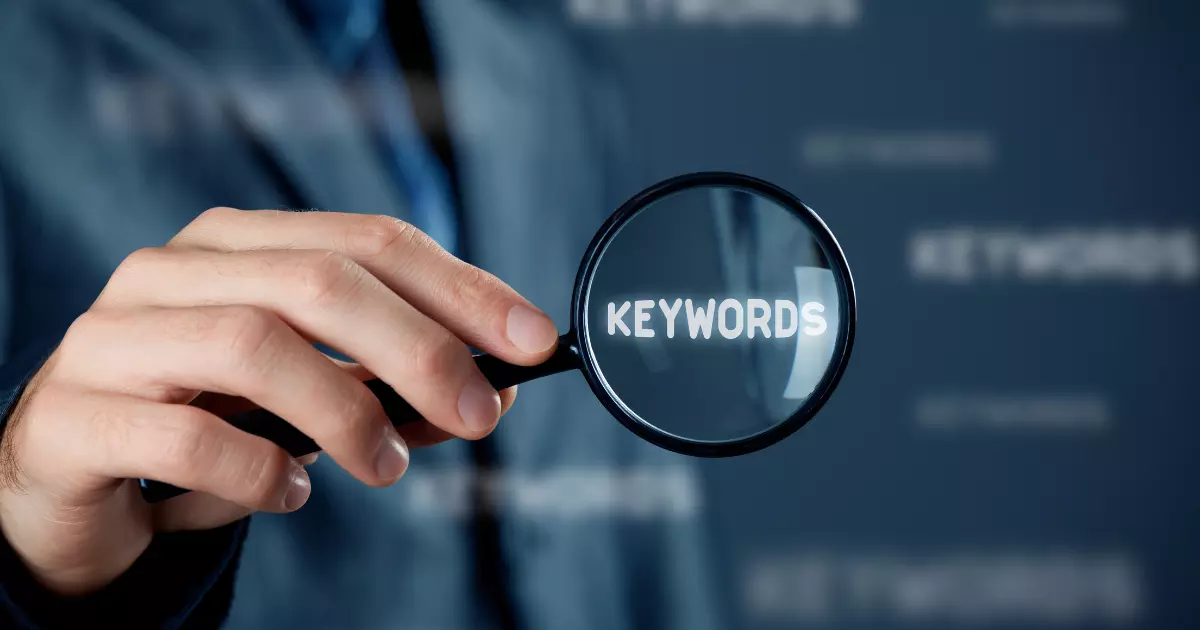 A close up of a hand holding a magnifying glass over the word KEYWORDS emphasizing the role of long tail keywords in targeted search engine optimization