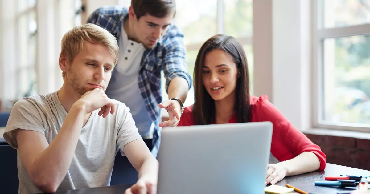 Three colleagues brainstorming video marketing ideas together while reviewing campaign content on a laptop